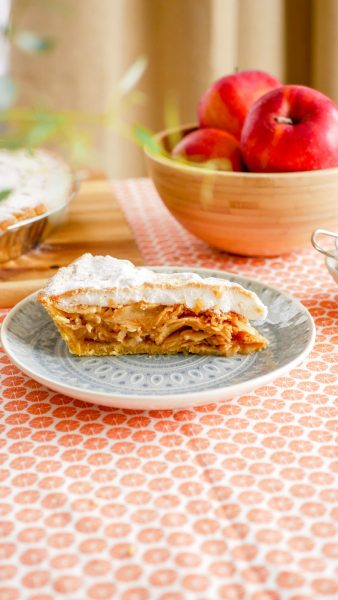 Habos almás pite szelet tálalva, a háttérben piros almákkal