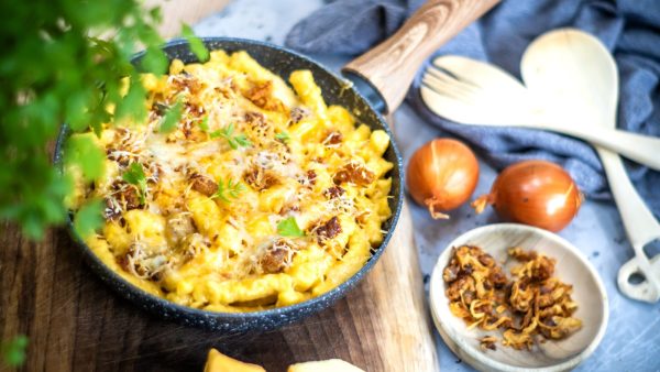 Käsespätzle tálalva hagymával és fakanállal